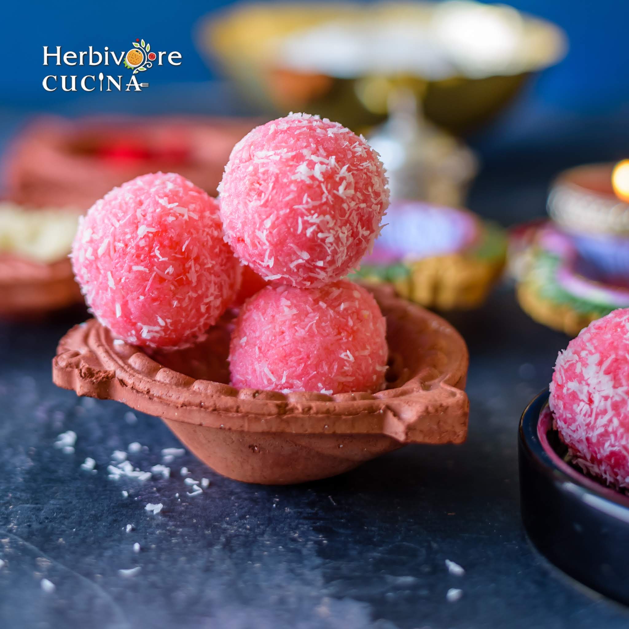 Coconut Strawberry Balls placed on a terracotta container with diyas on the sides.