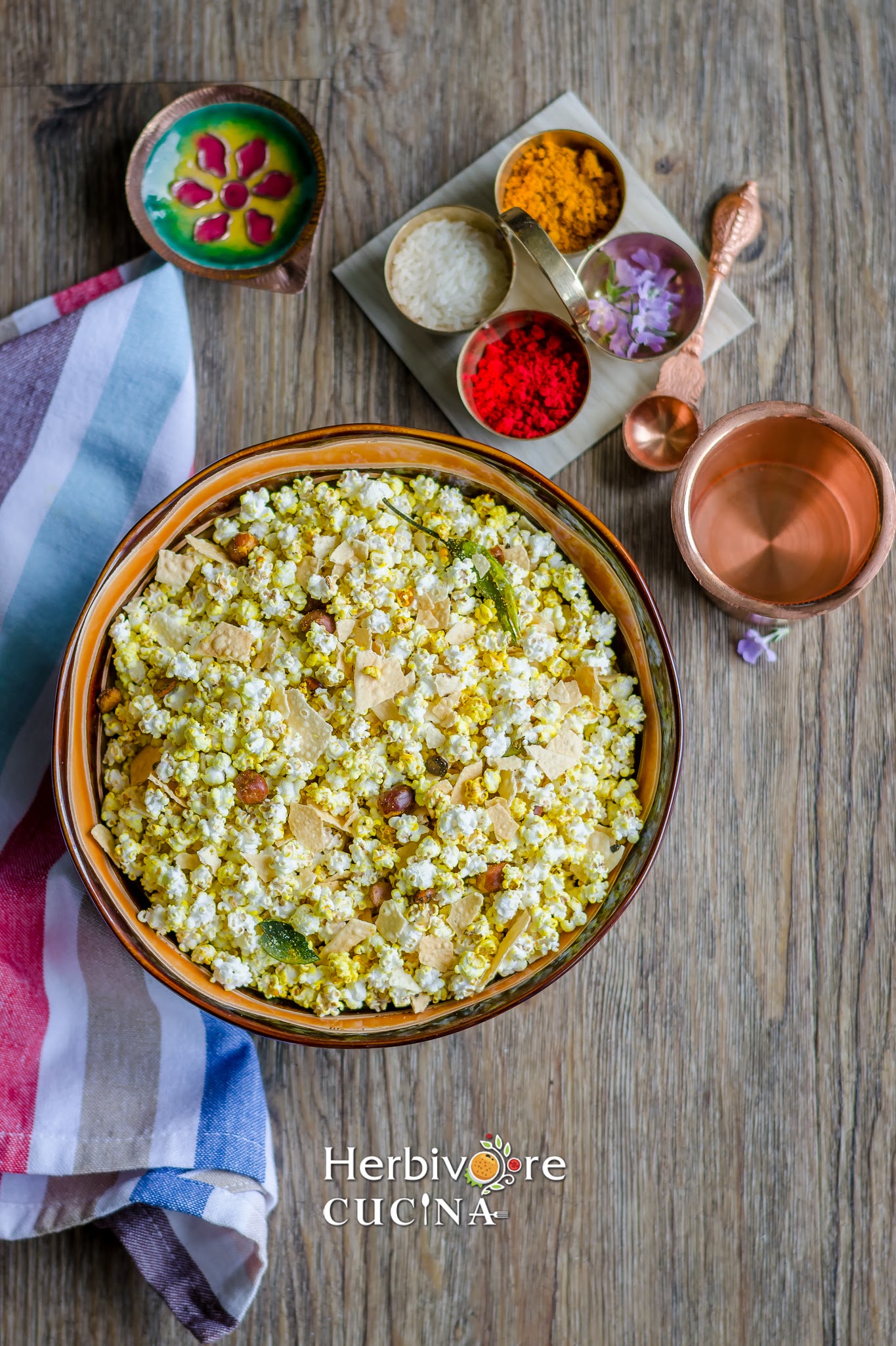 A brown bowl filled with jowar dhani chivda and all the parts of pooja thali around it. 