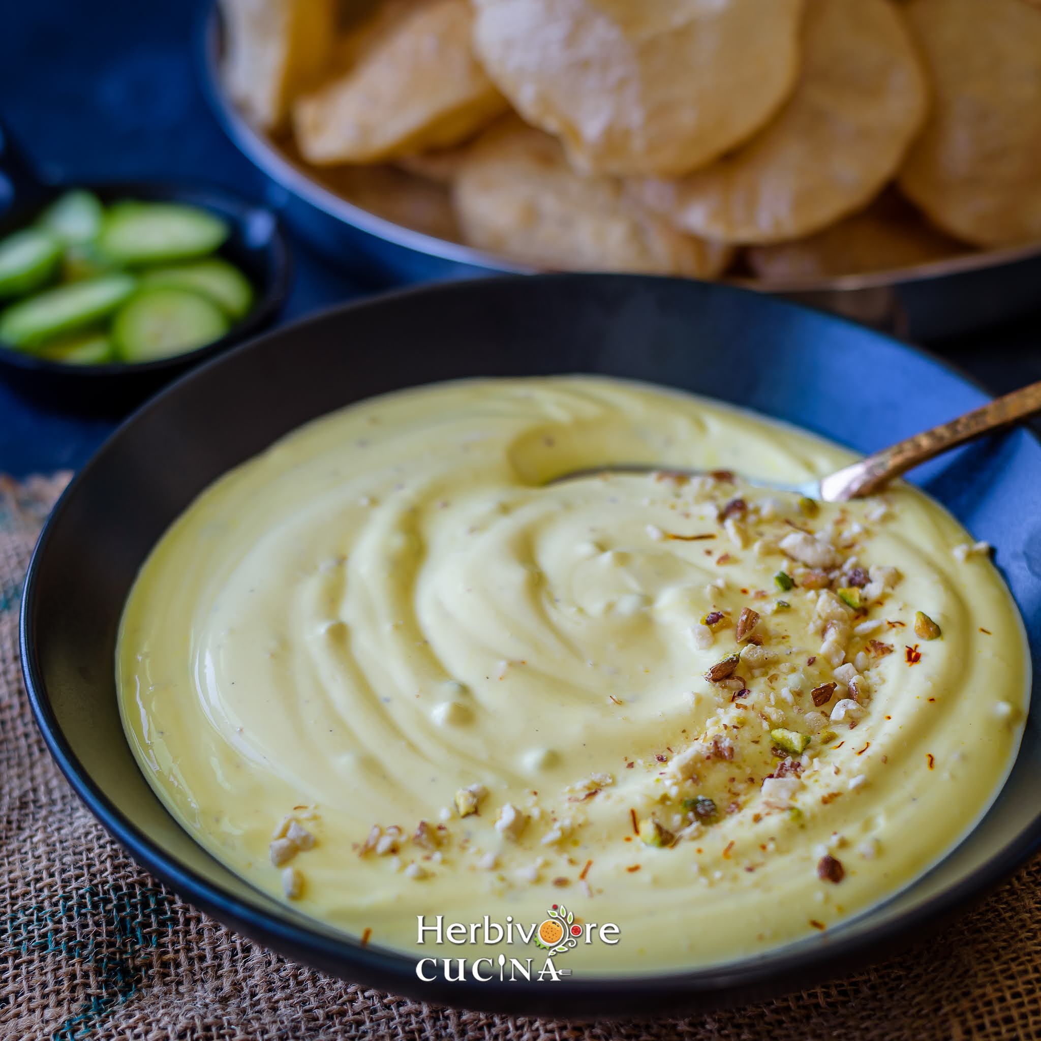 A black bowl filled with Kesar Shrikhand with some puris in the background. 