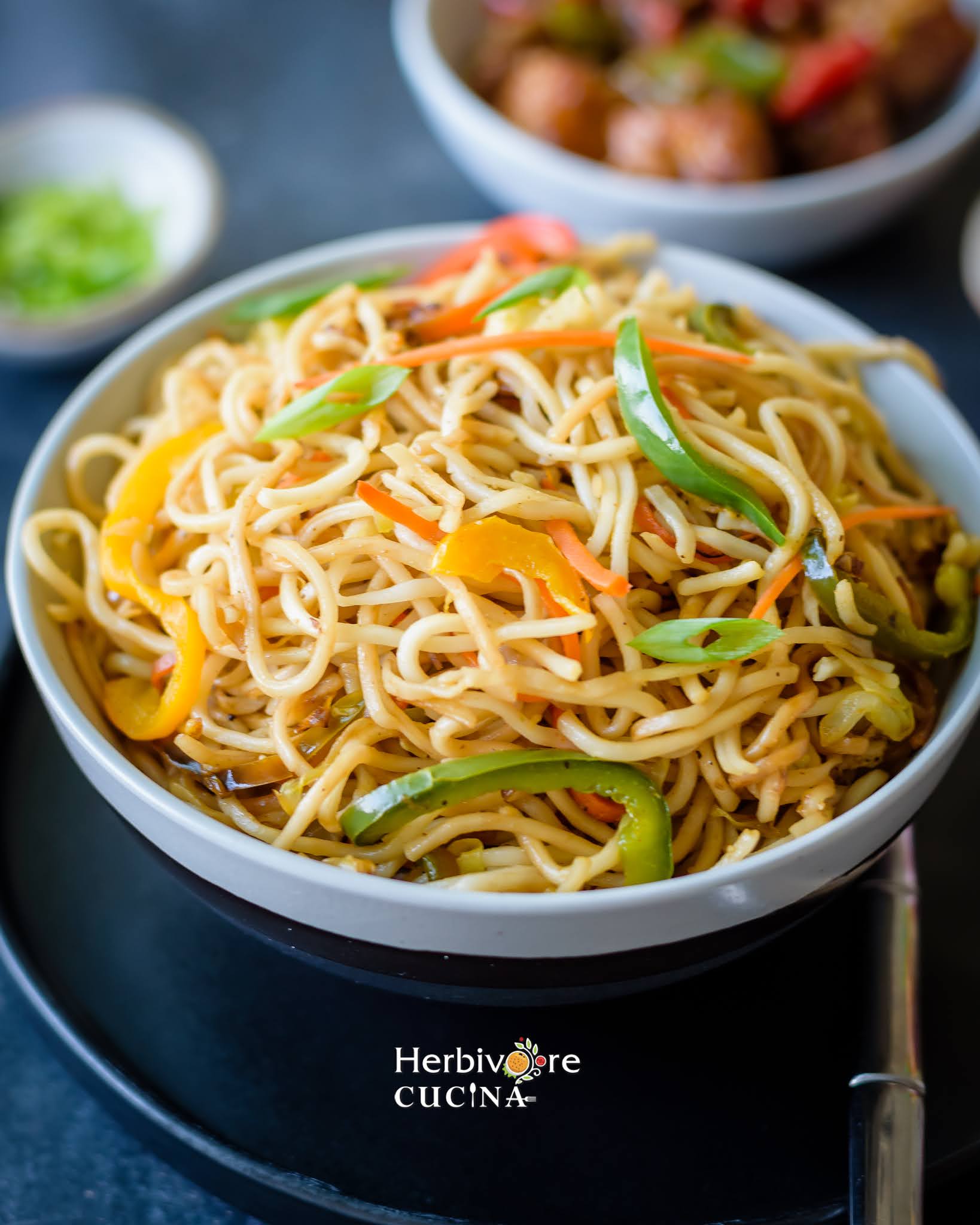 Vegetarian Hakka Noodles in a bowl shot from the side with a fork and plate on the side.
