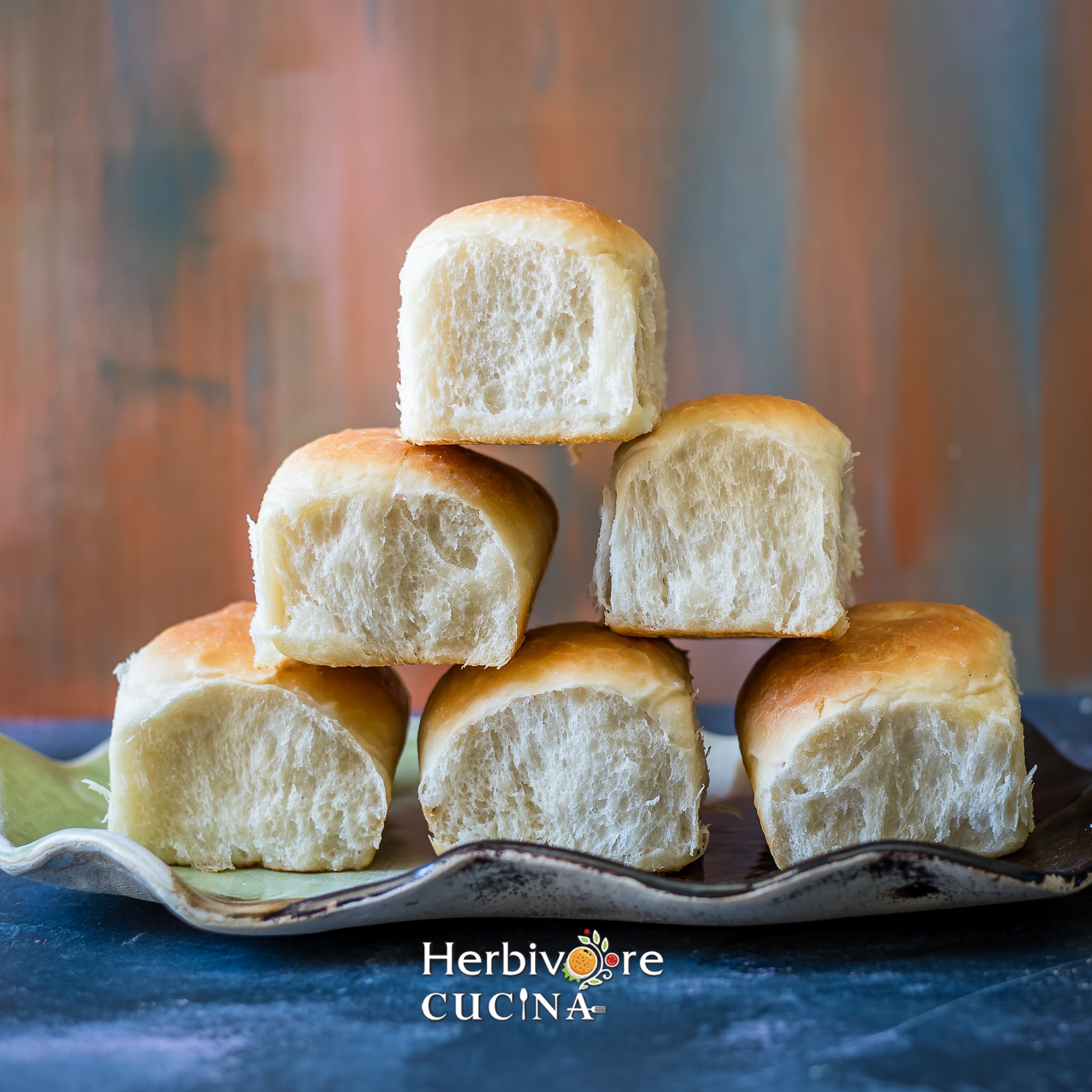 Vegan bread rolls arranged in a pyramid shape in a tray against a blue brown backdrop. 