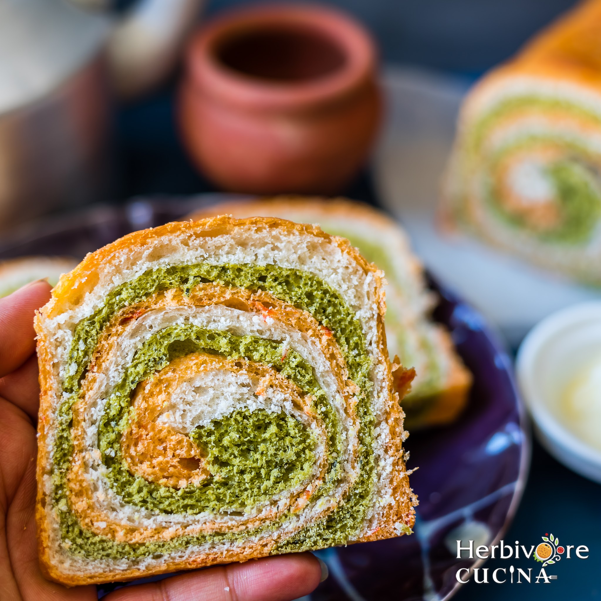 Holding a slice of tricolor bread against a dark background with chai cups on the side. 