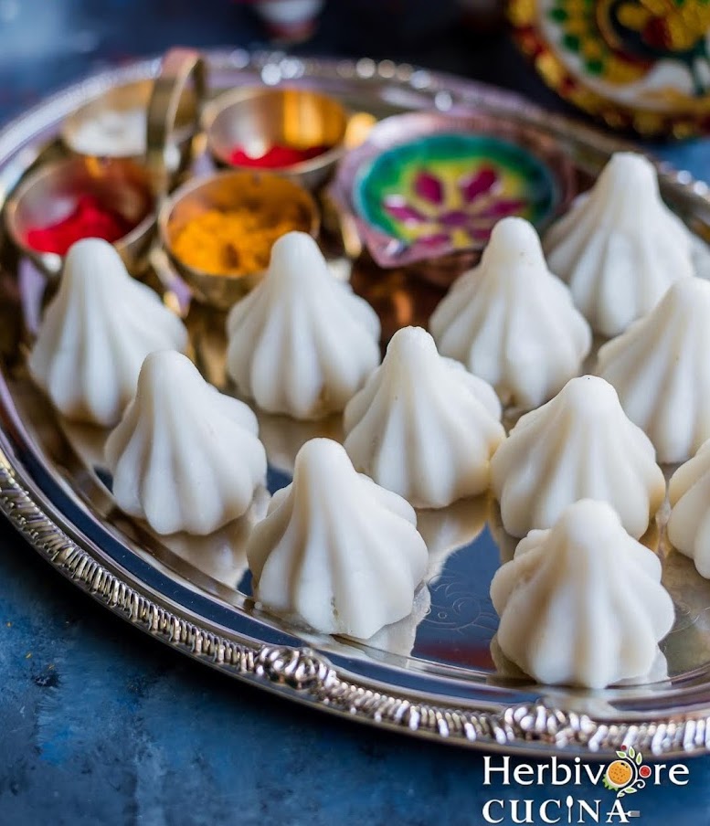 A large steel platter with ukadiche modak with diya and pooja elements around it. 