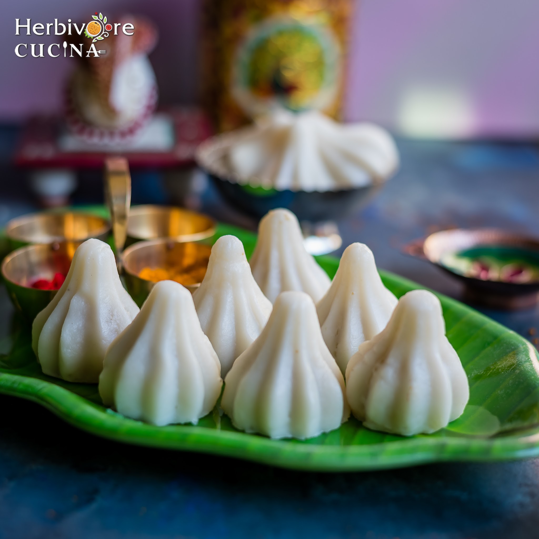 Green plate with steamed Ukadiche Modak with Ganesha idol and more decor items in the background.