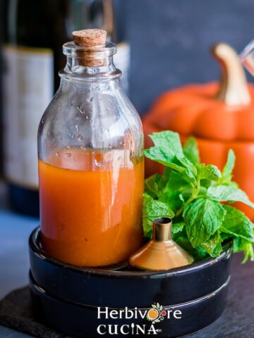 Pumpkin simply syrup in a glass bottle; with mint leaves, a funnel and glasses around it.