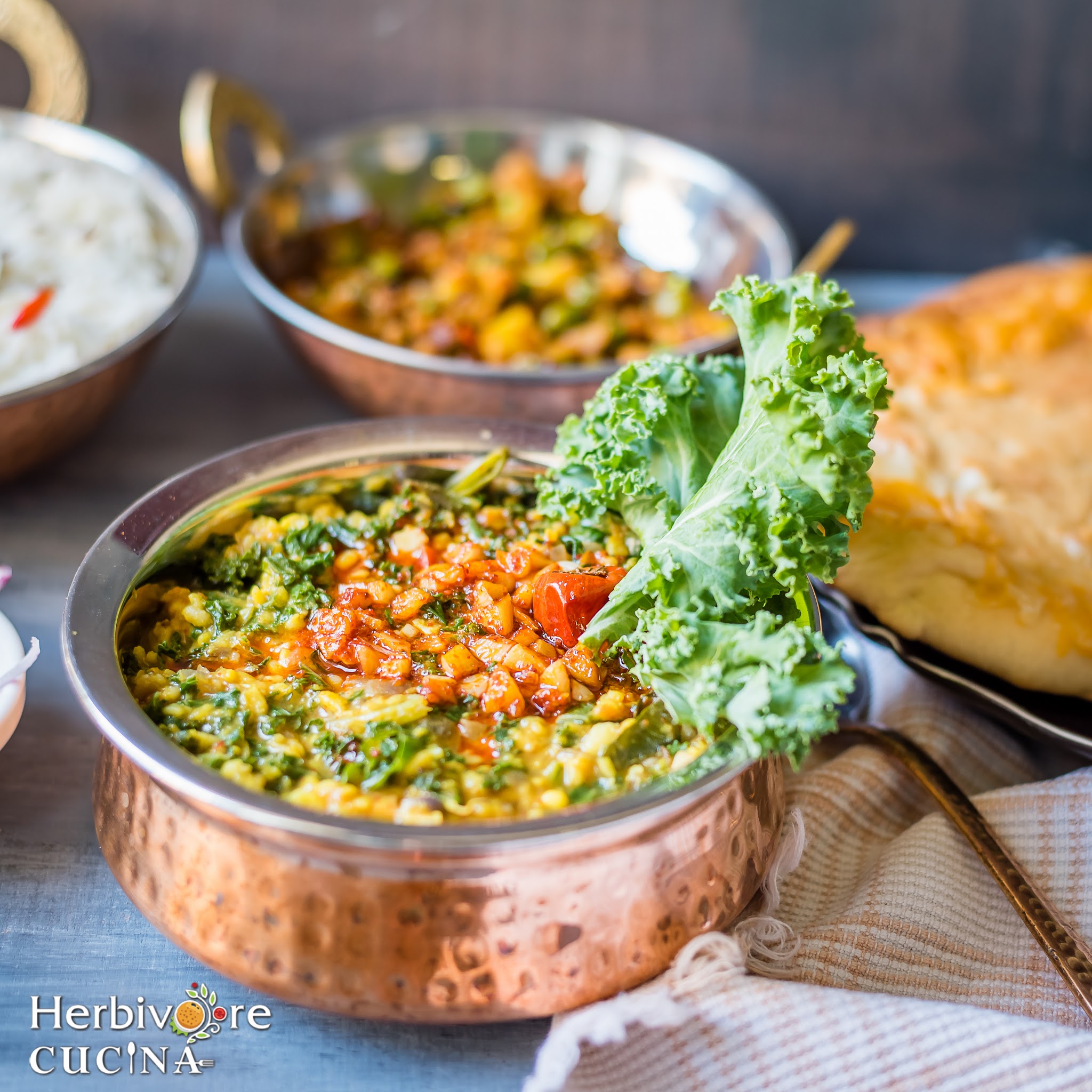 A copper kadhai filled with Kale and moong Dal and tempered with garlic; served along with some steamed rice, naan and vegetable.
