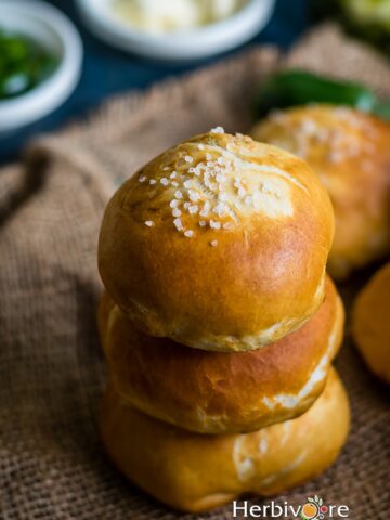 A stack of pretzel buns with the ingredients on the side of a brown background.