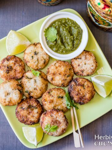 A square green plate with samo fritters served with cilantro chutney in a bowl and some lemon wedges beside it.