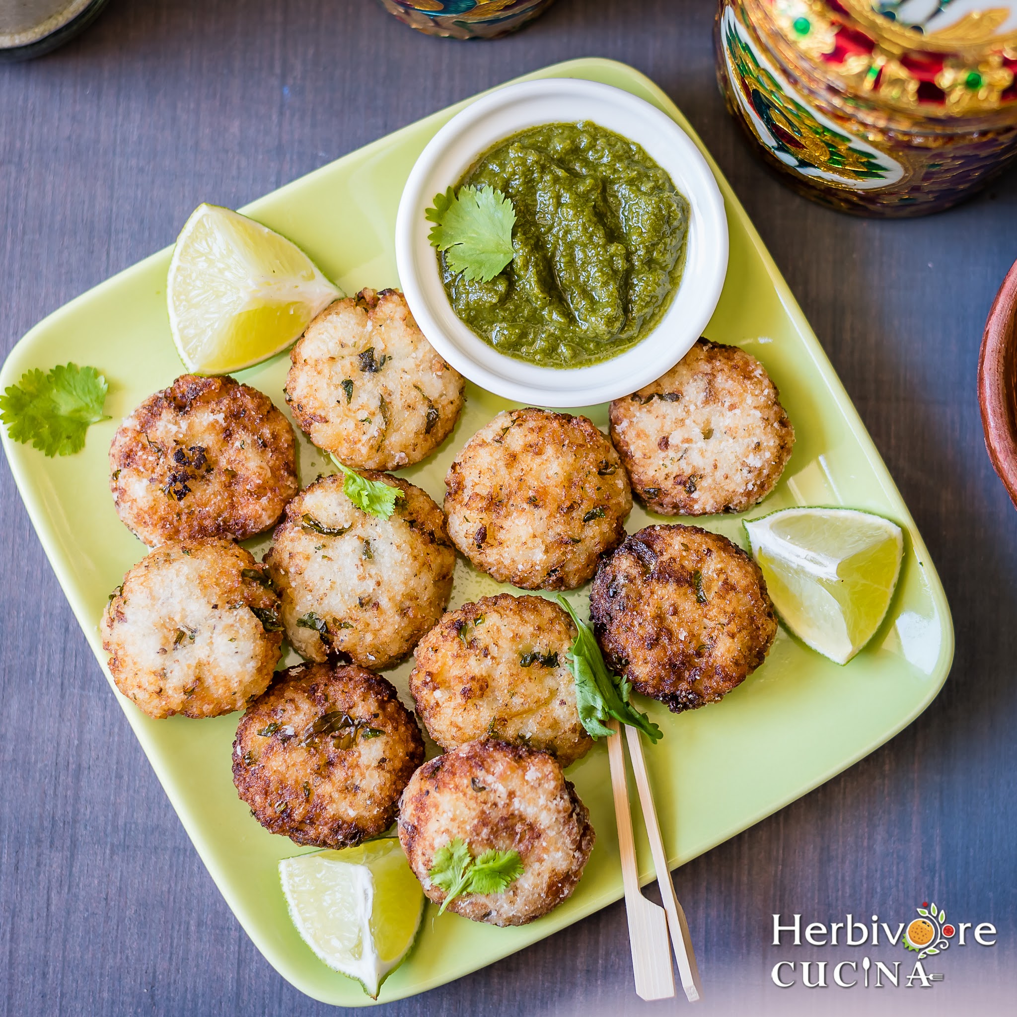 A green square plate with barnyard fritters served with cilantro chutney and lemon wedges. 