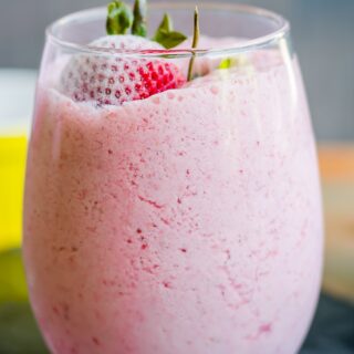 A glass with strawberry milkshake topped with whole strawberries.