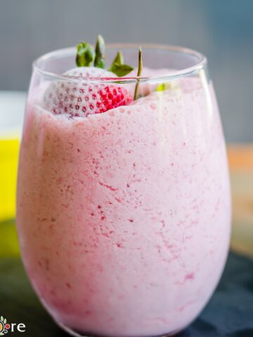 A glass with strawberry milkshake topped with whole strawberries.