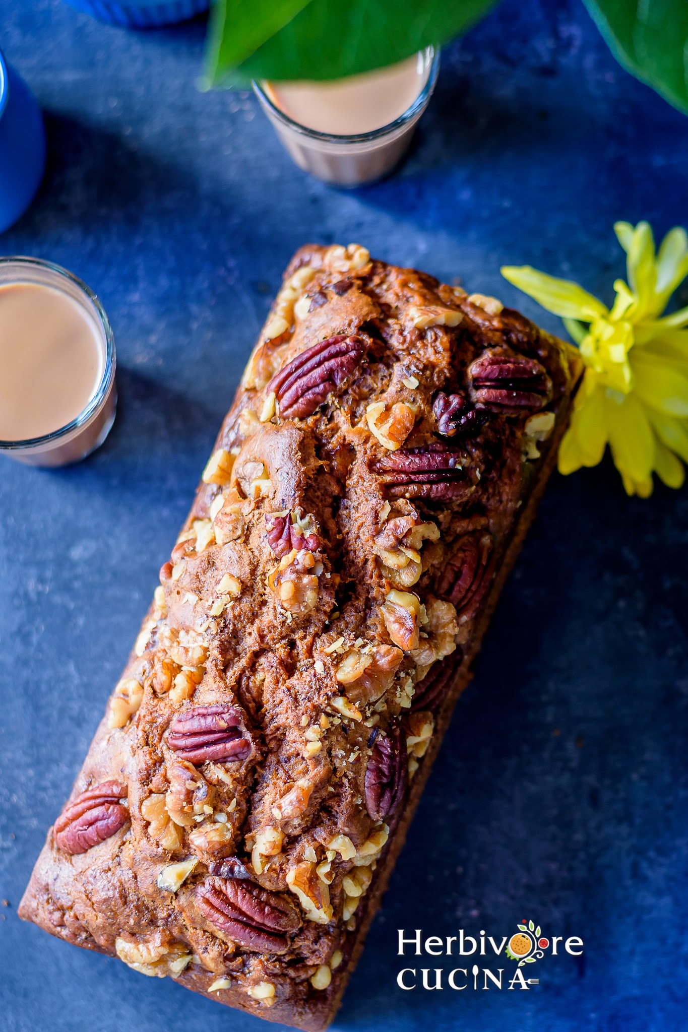 A loaf of Starbucks Banana Nut bread with coffee on the side and some flowers on a dark board.