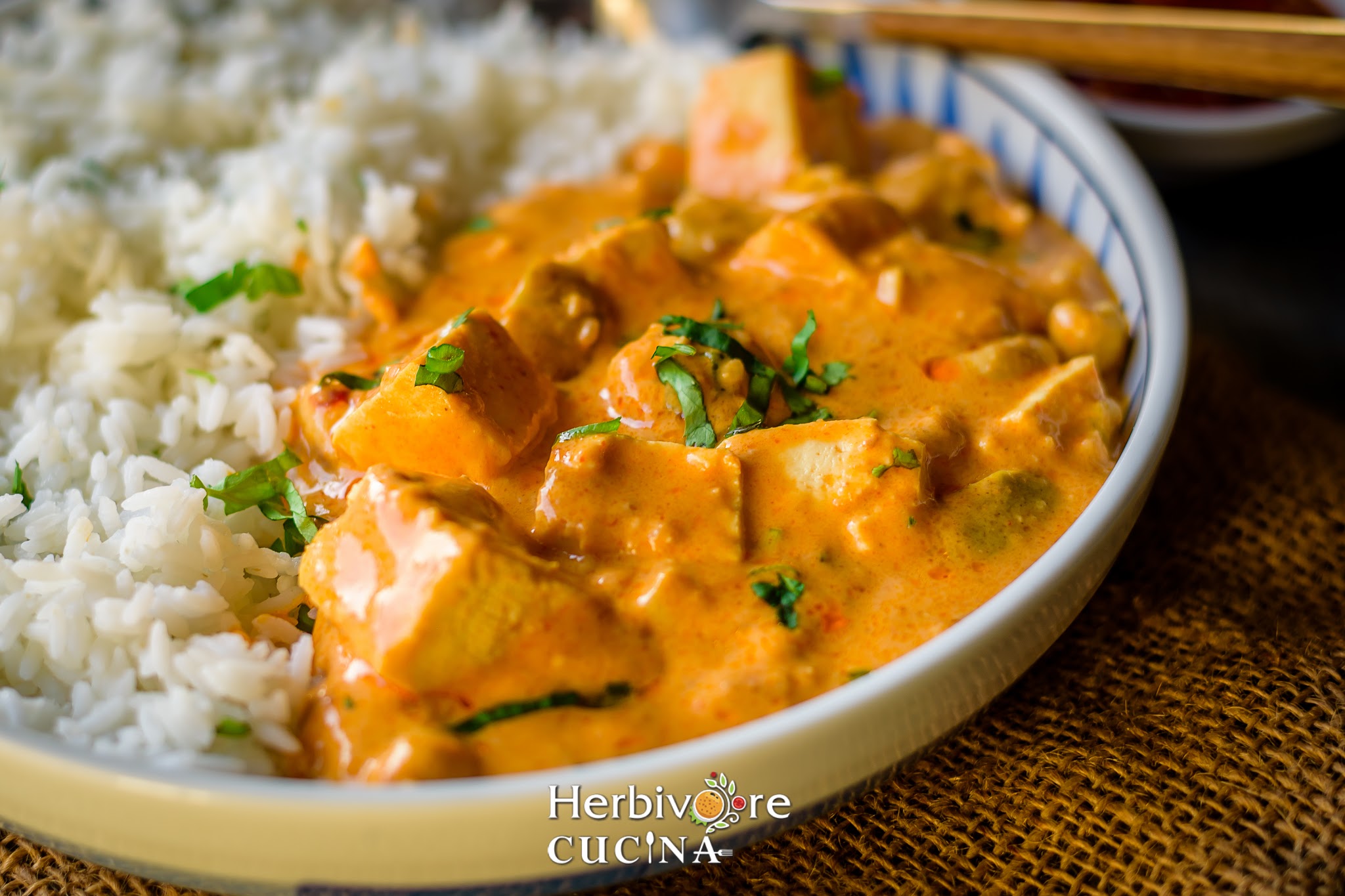 Side view of peanut based tofu dish in a plate with steamed rice placed next to it and sprinkled with cilantro. 