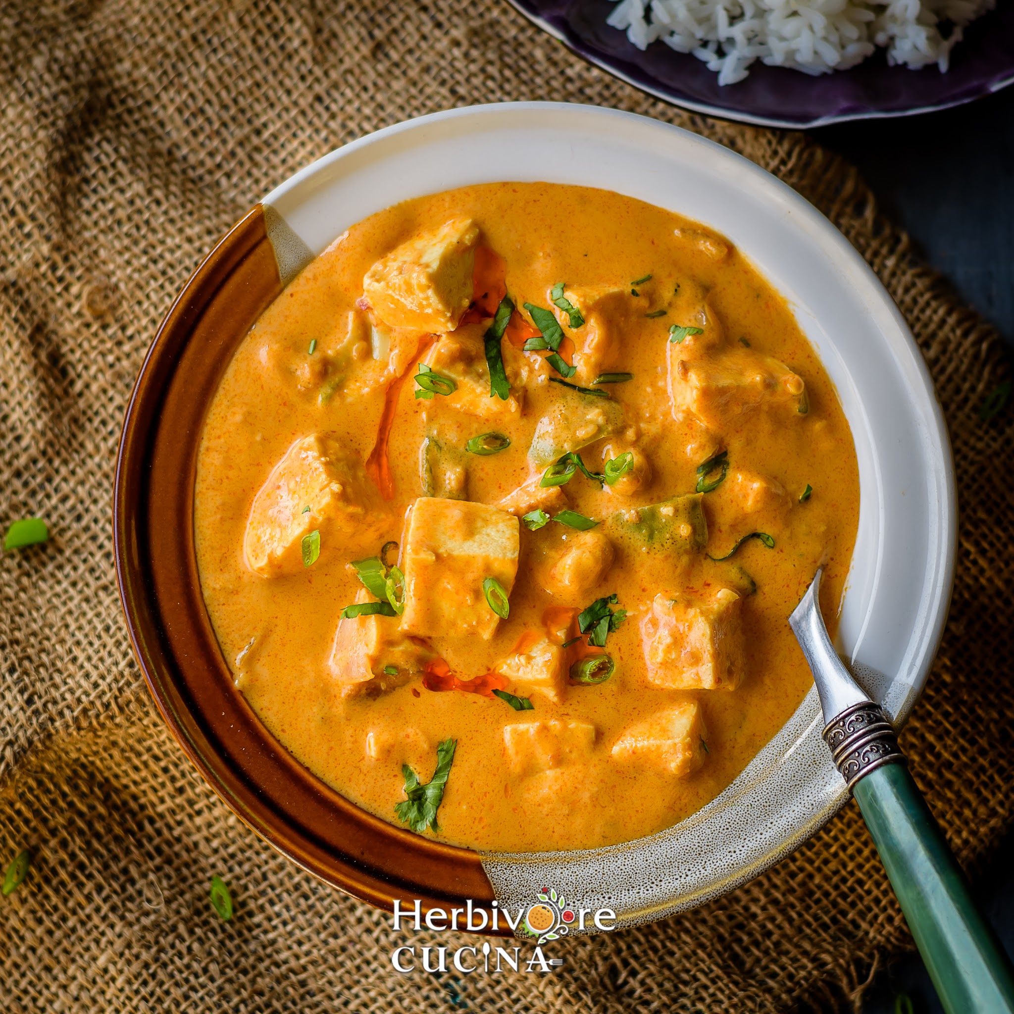 A white bowl with tofu curry made with peanut butter and coconut milk served with steamed rice in a purple plate. 