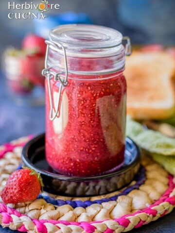A glass jar filled with strawberry chia jam and some berries on the side.