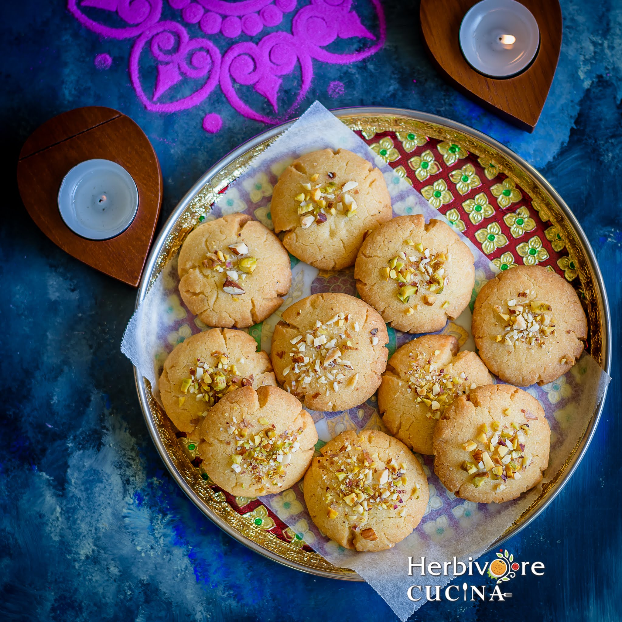 A gold red plate filled with nut studded nankhatai; arranged in a pile on a parchment paper.