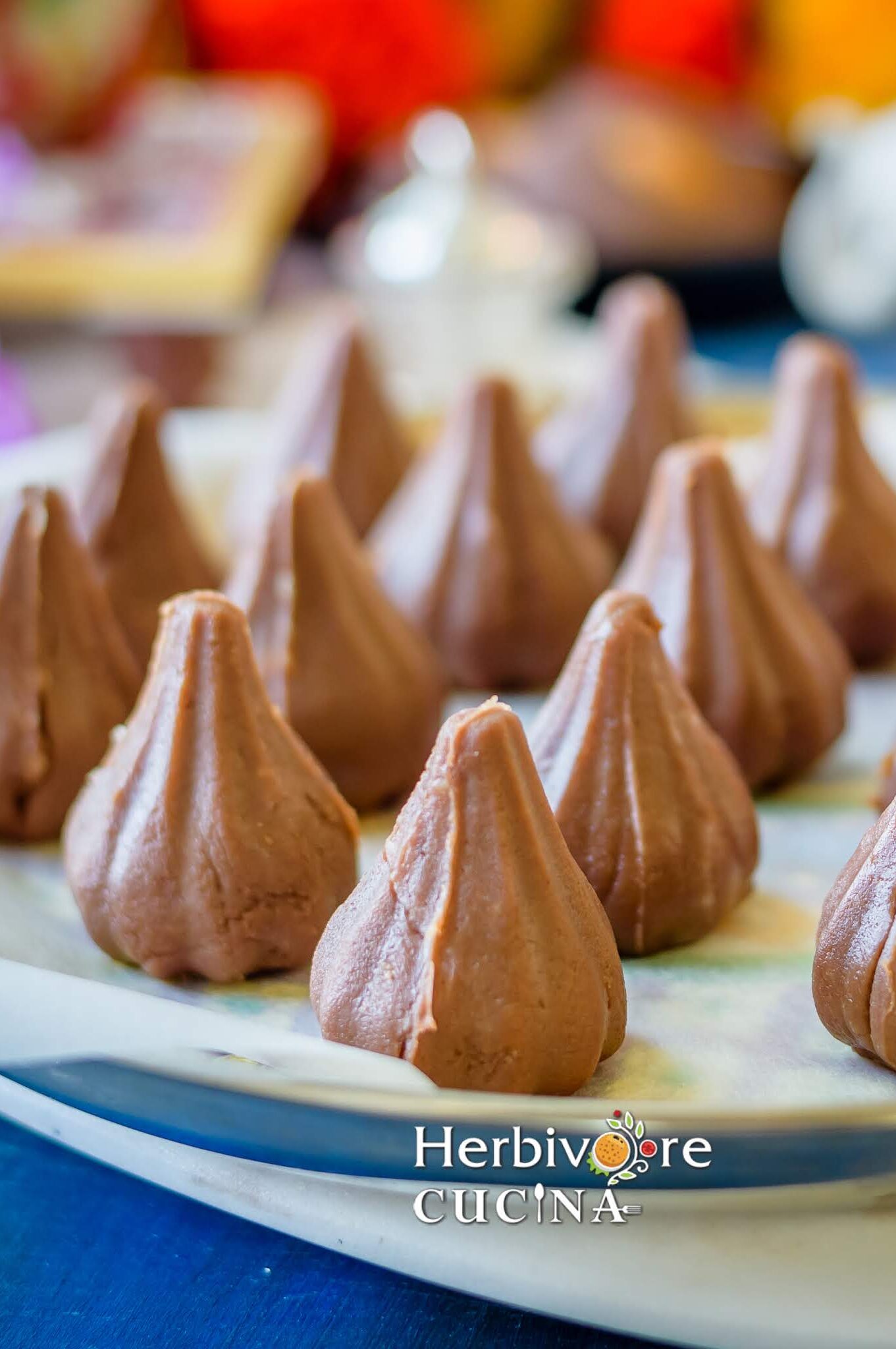 Chocolate modak on a plate with flowers and other ingredients on the side.
