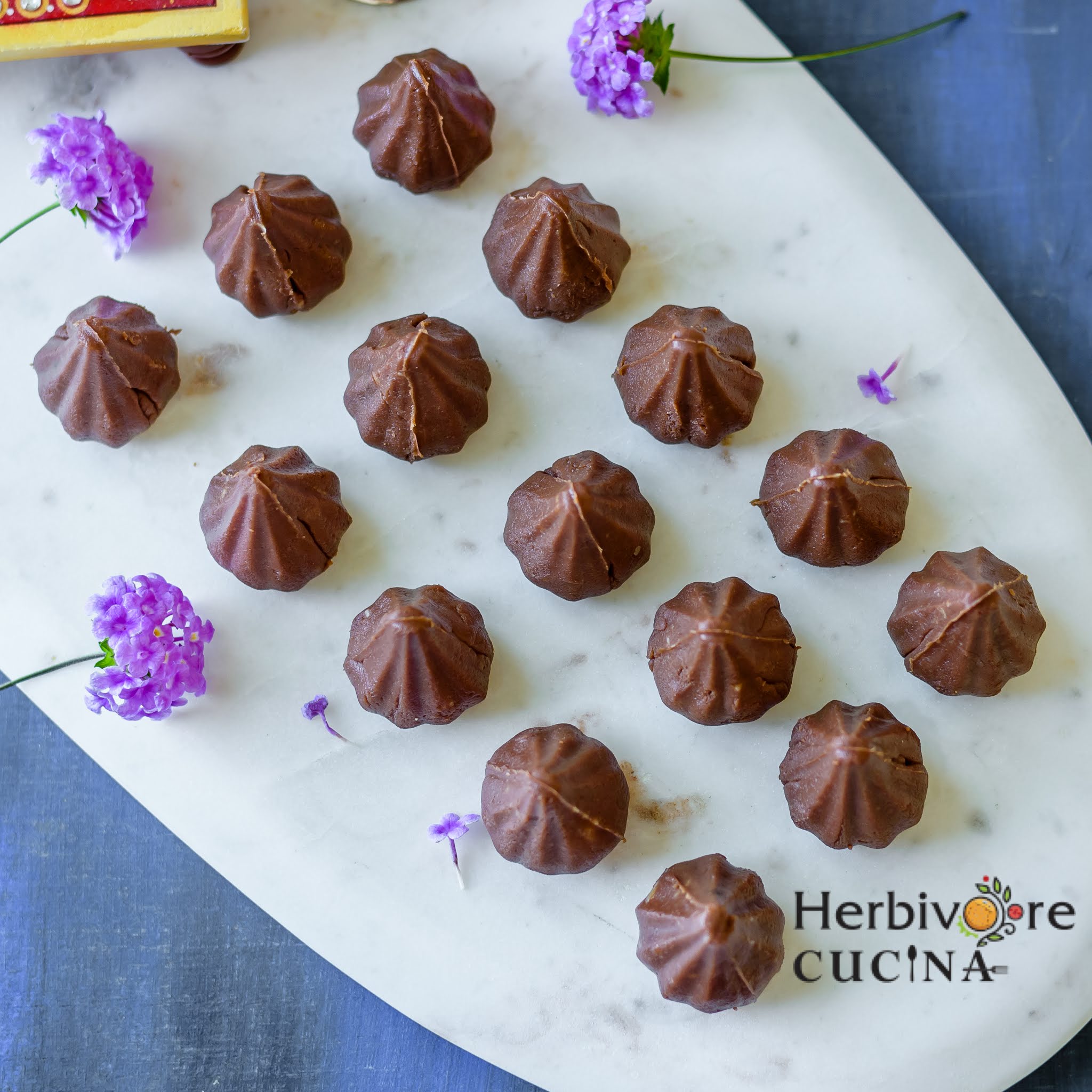 Chocolate modak on a marble platter with purple flowers around it. 