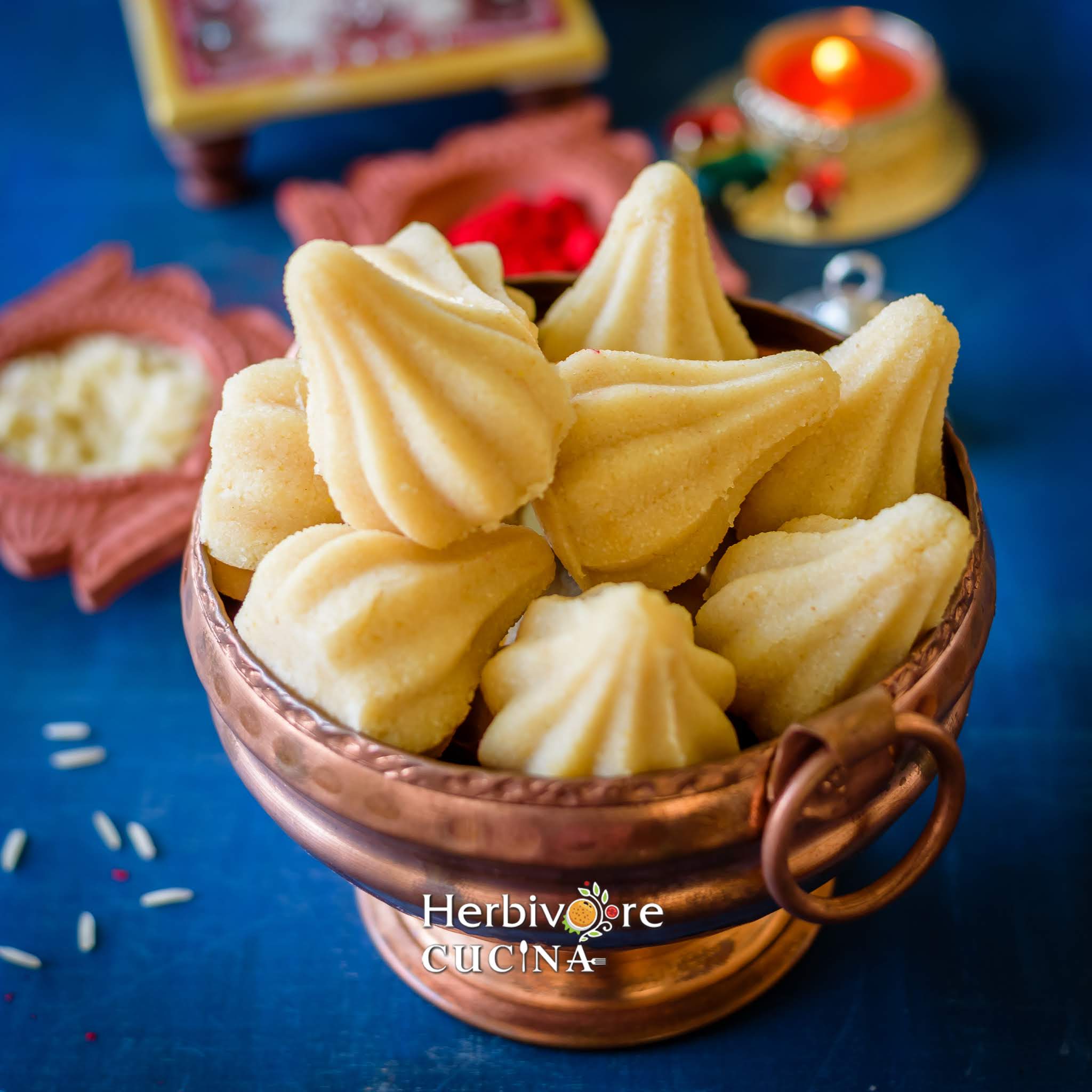 A copper utensil filled with semolina modak in it with Ganesha in the background.