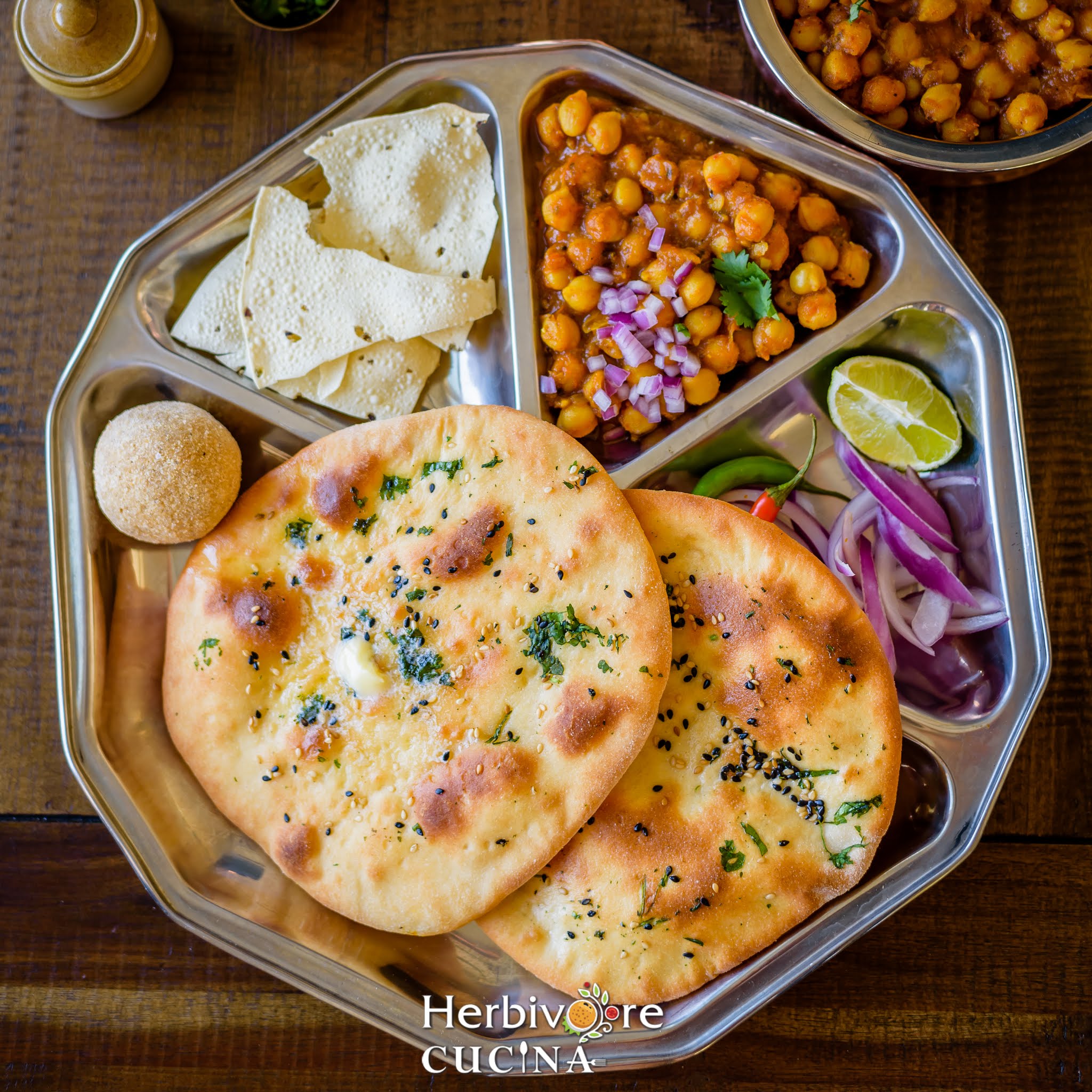 A platter with chole, kulcha, ladoo, papad and salad. 