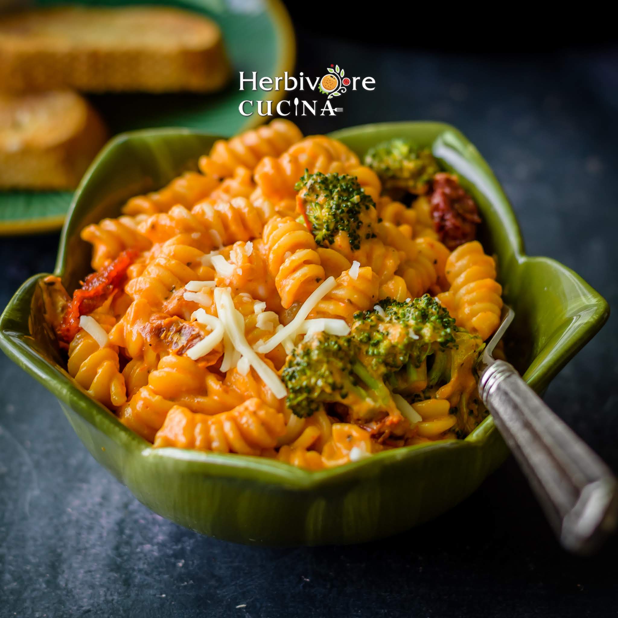 A green bowl with pasta in creamy red sauce with broccoli florets on top and served with a fork.