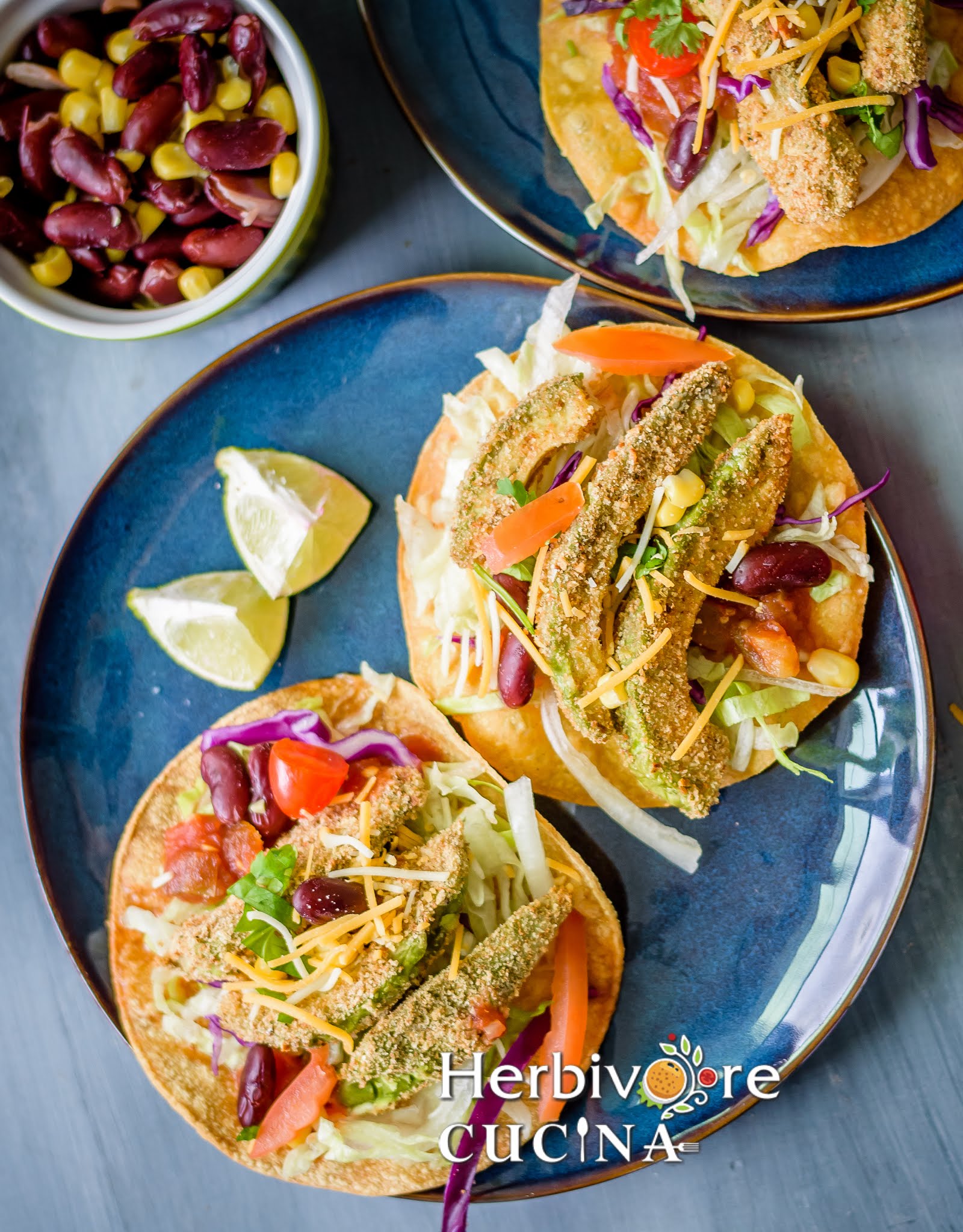 A blue plate with avocado fries tostada and other toppings with lemon slice on the side.