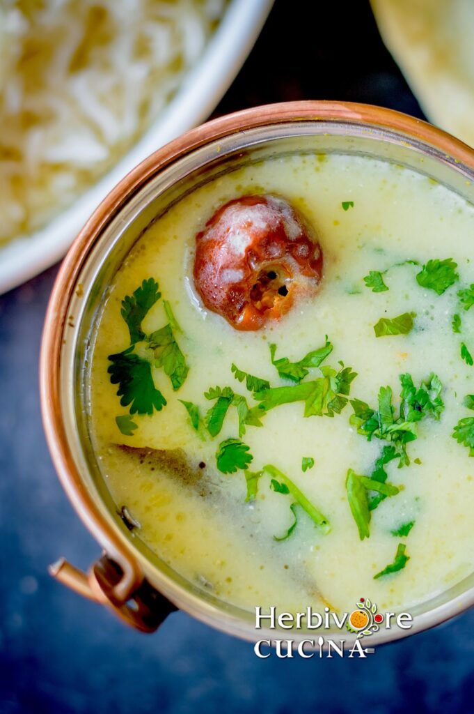 Top view of Gujarati Kadhi served in a copper bowl with rice and papad on the side.