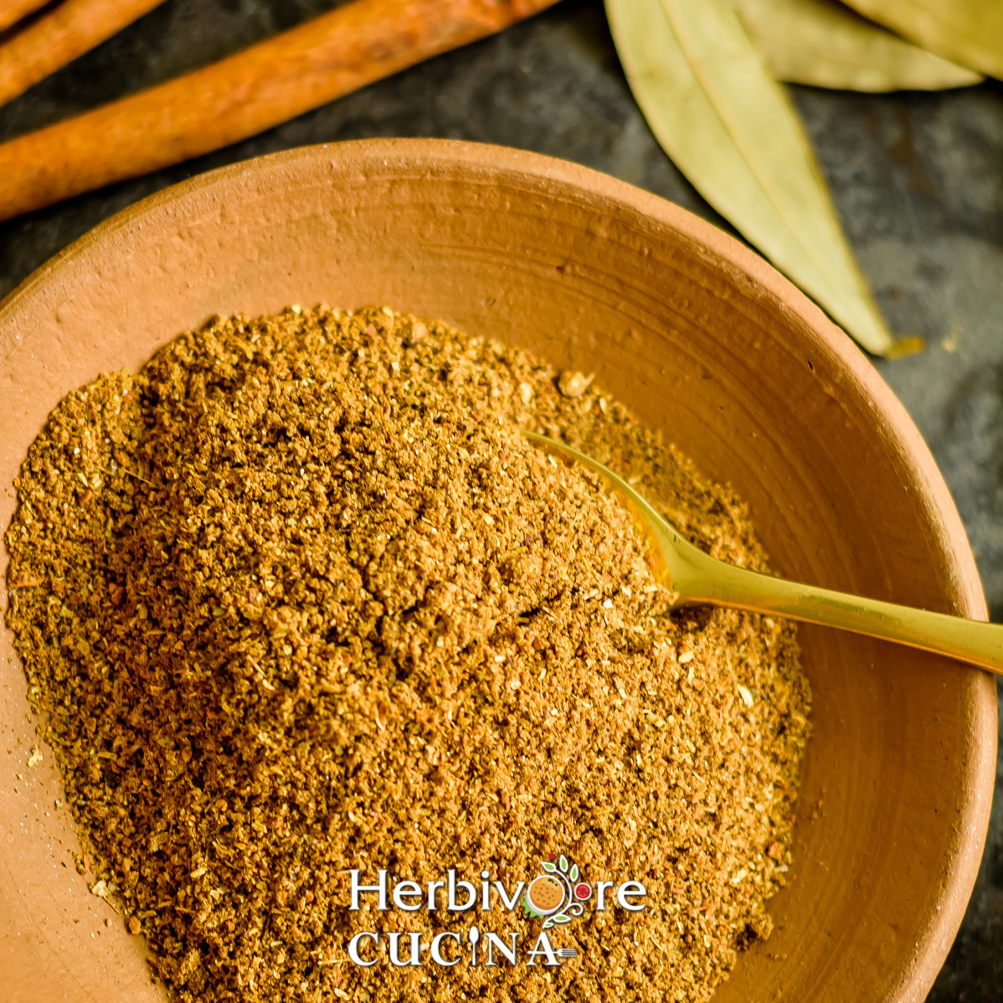  A brown plate with garam masala in it and a golden spoon placed in the masala on the side. 