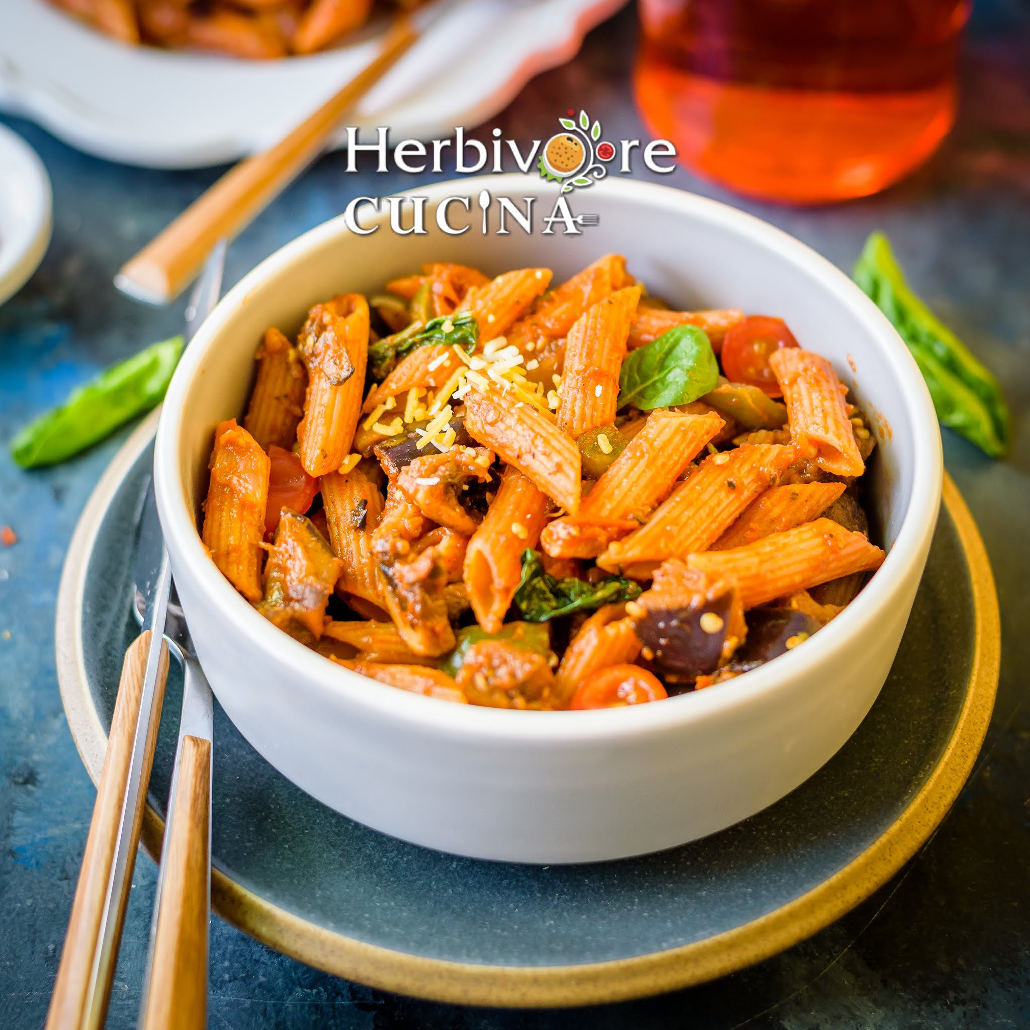 A gray plate with gray bowl filled with Sicilian Eggplant Mushroom Penne with for and spoon on the side.