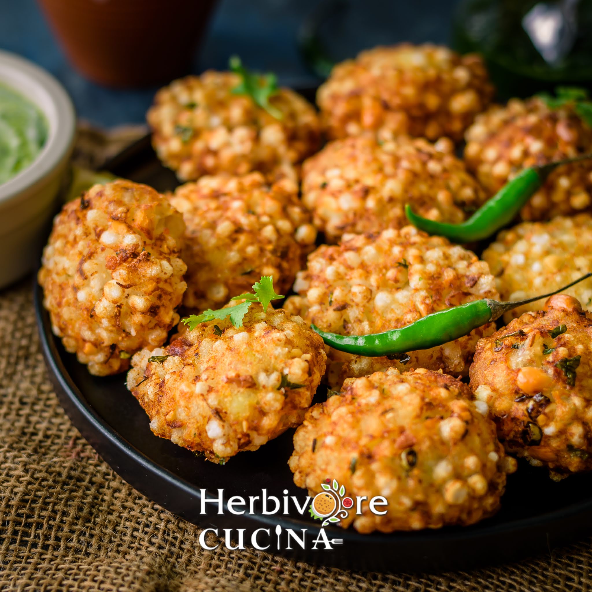 Side view of sabudana vada in a black plate with green chili and cilantro. 