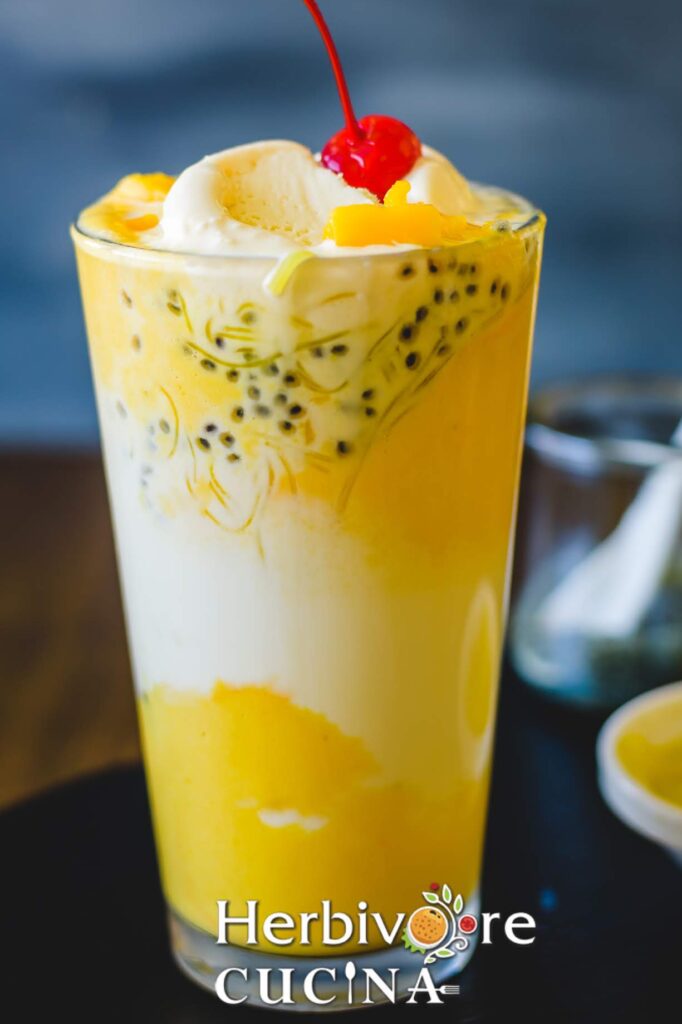 A glass filled with a delicious mango drink or dessert; with sabja seeds, ice cream and cherry on top.