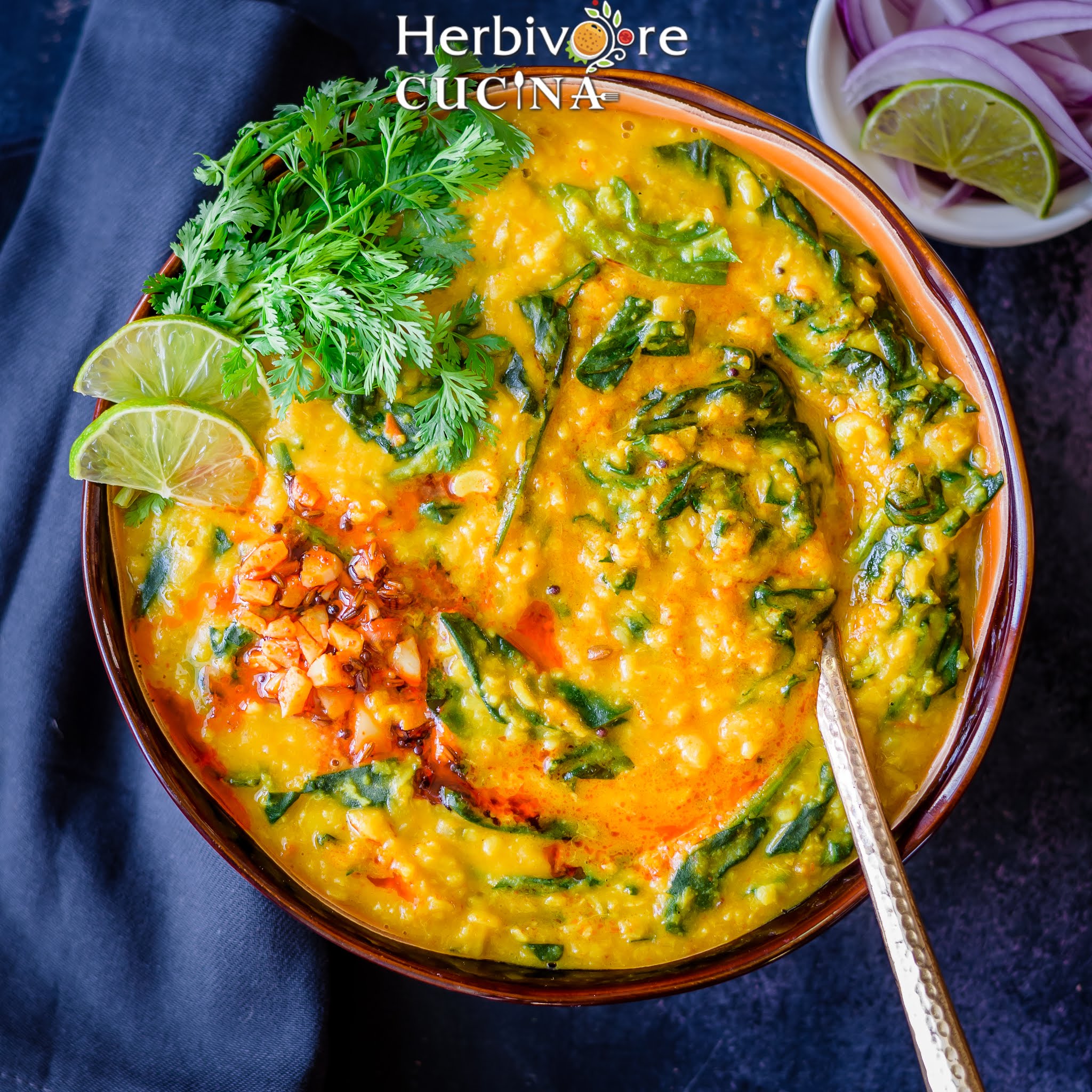 A brown bowl with dal palak with tadka on top; with cilantro and a spoon beside it.