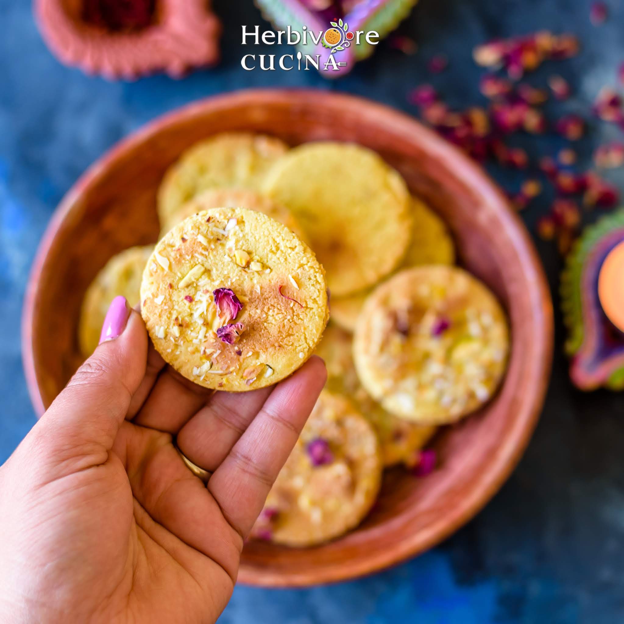 A badam puri held in the hand above a platter full of these cookies.