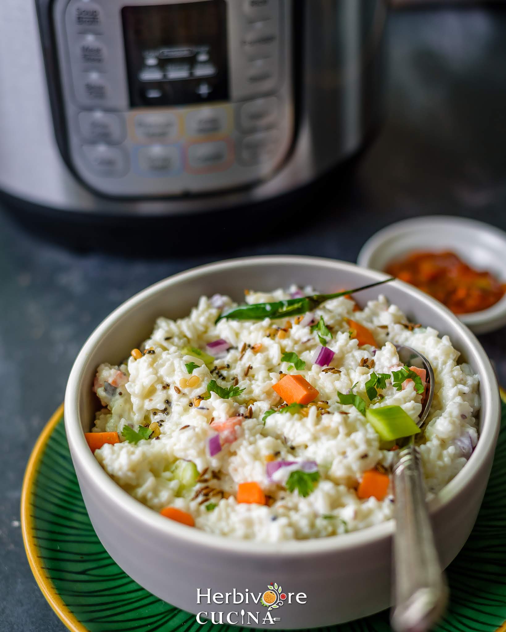 Gray bowl filled with Instant Pot Yogurt Rice in a green plate served with a steel spoon.