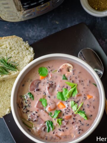 A bowl filled with wild rice and mushroom soup served with sliced bread and an instant pot by the side.