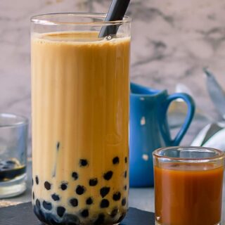 Boba Tea in glass with a black straw in it and some brewed tea and a small jug with milk beside it.