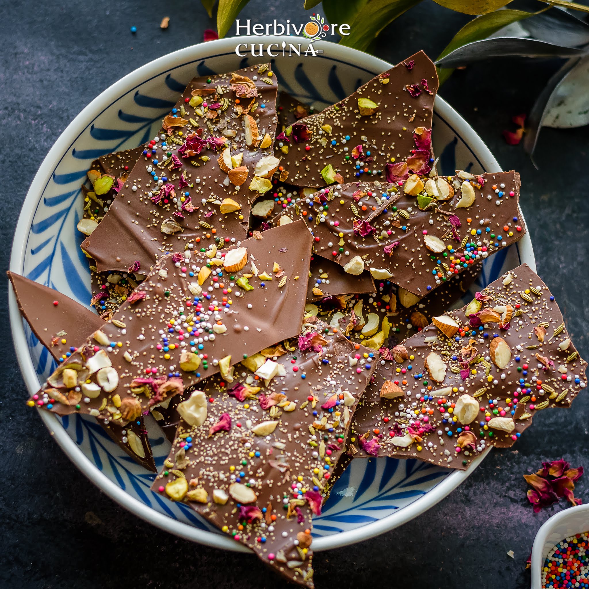 Chocolate bark with nuts, sprinkles, fennel and rose petals in a white blue plate.