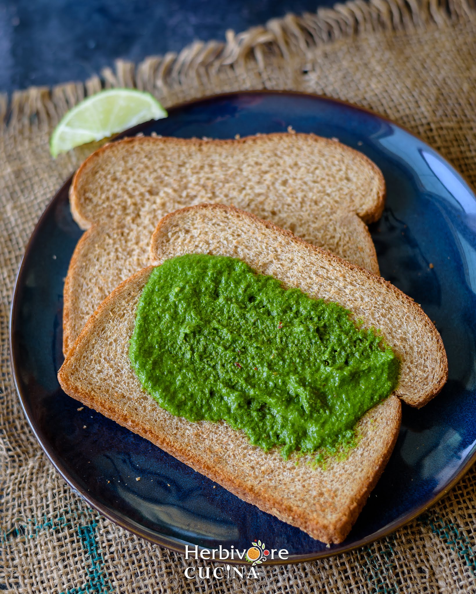 A blue plate with two slices of bread topped with cilantro chutney placed on a brown background. 