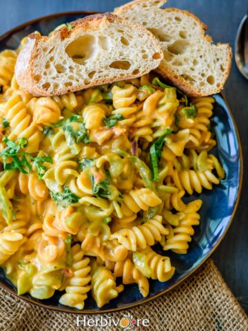 A blue plate filled with pumpkin sauce pasta and served with sliced bread on the side.