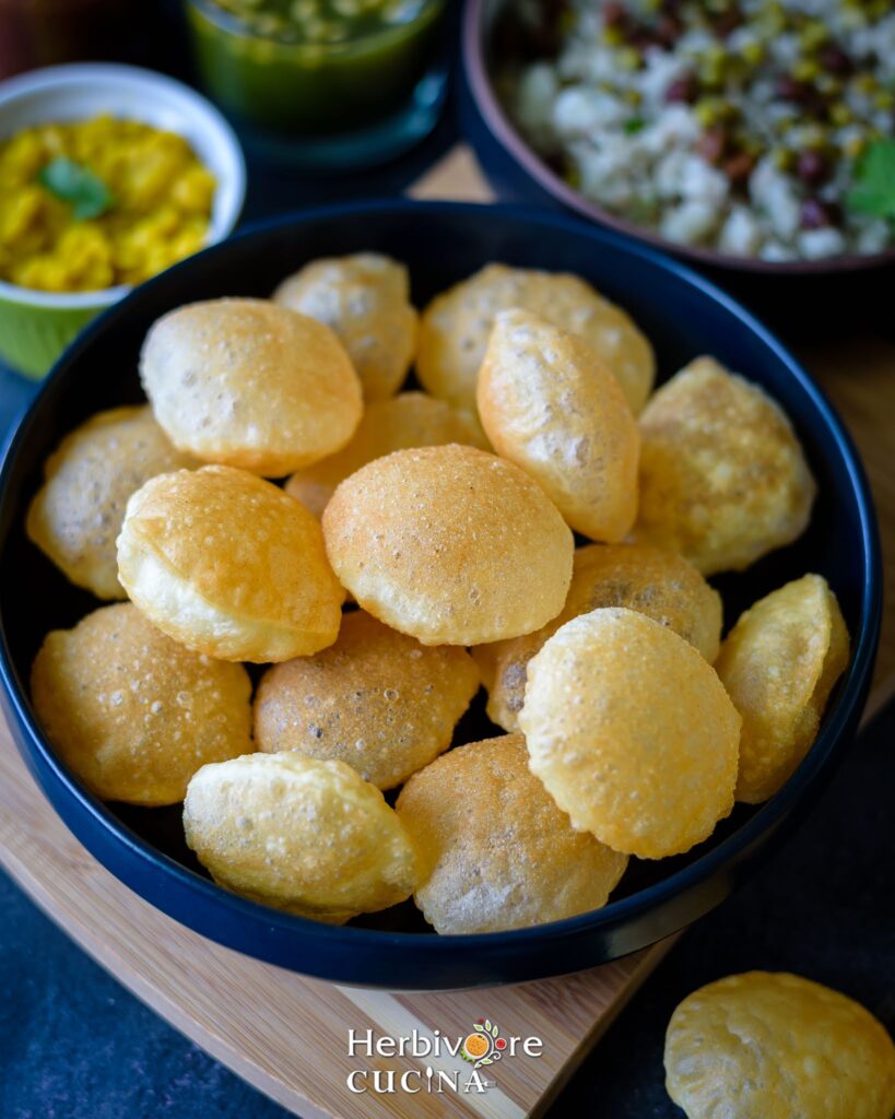 Blue platter with fried puris for pani puri and other chaats with more chaat ingredients around it.