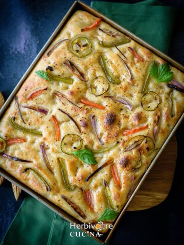 A rectangle tray with sourdough focaccia; topped with onions, peppers and jalapeños.