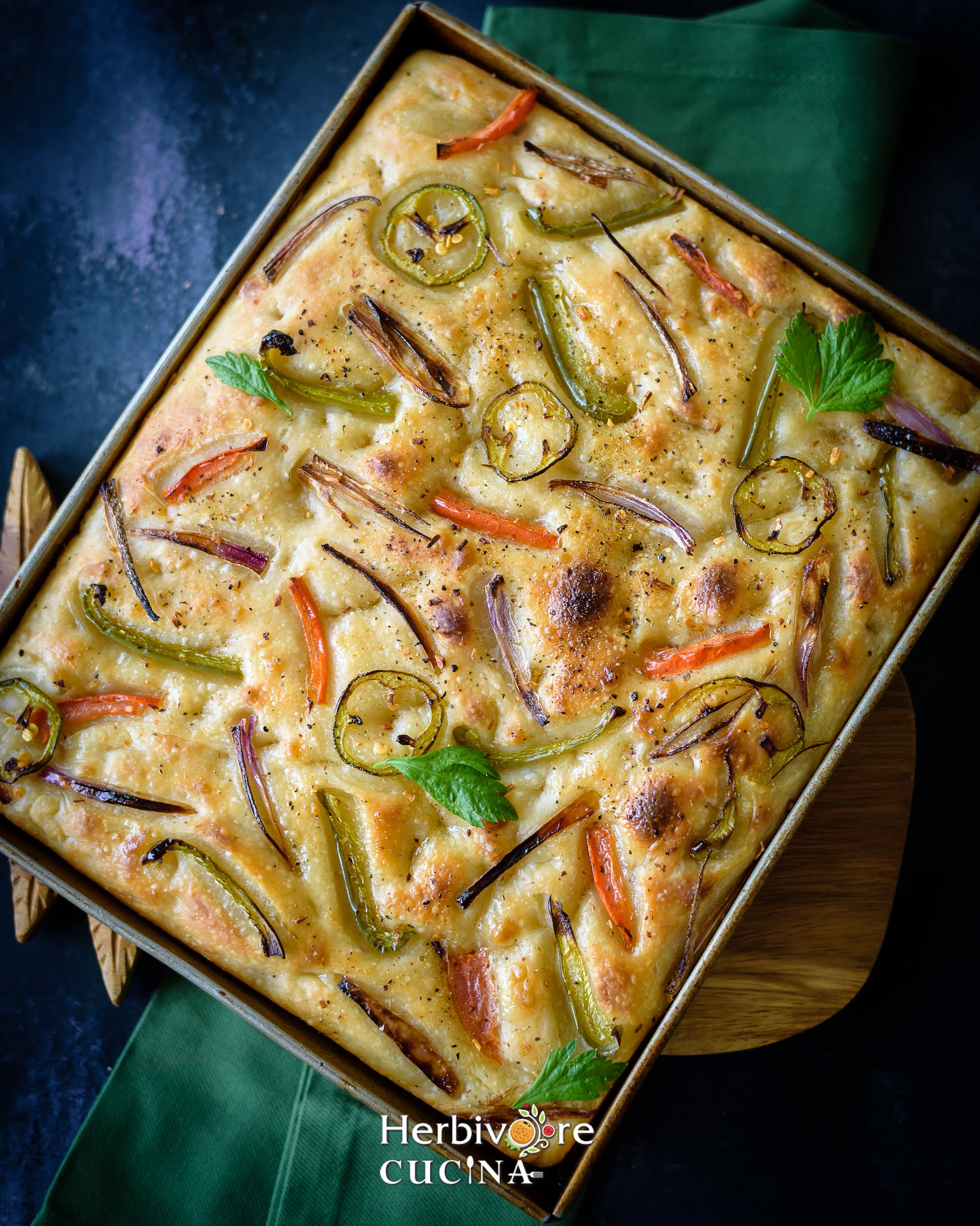 A large pan filled with baked sourdough focaccia; topped with peppers, onions and jalapeños. 