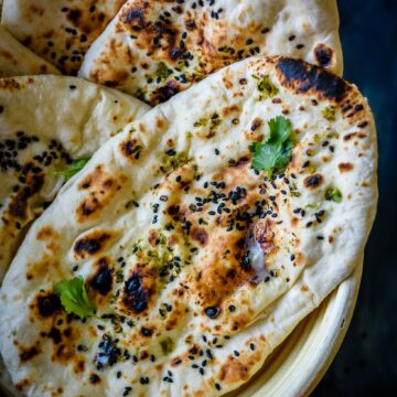 Sourdough naan placed in a basket, topped with cilantro and sesame seeds.