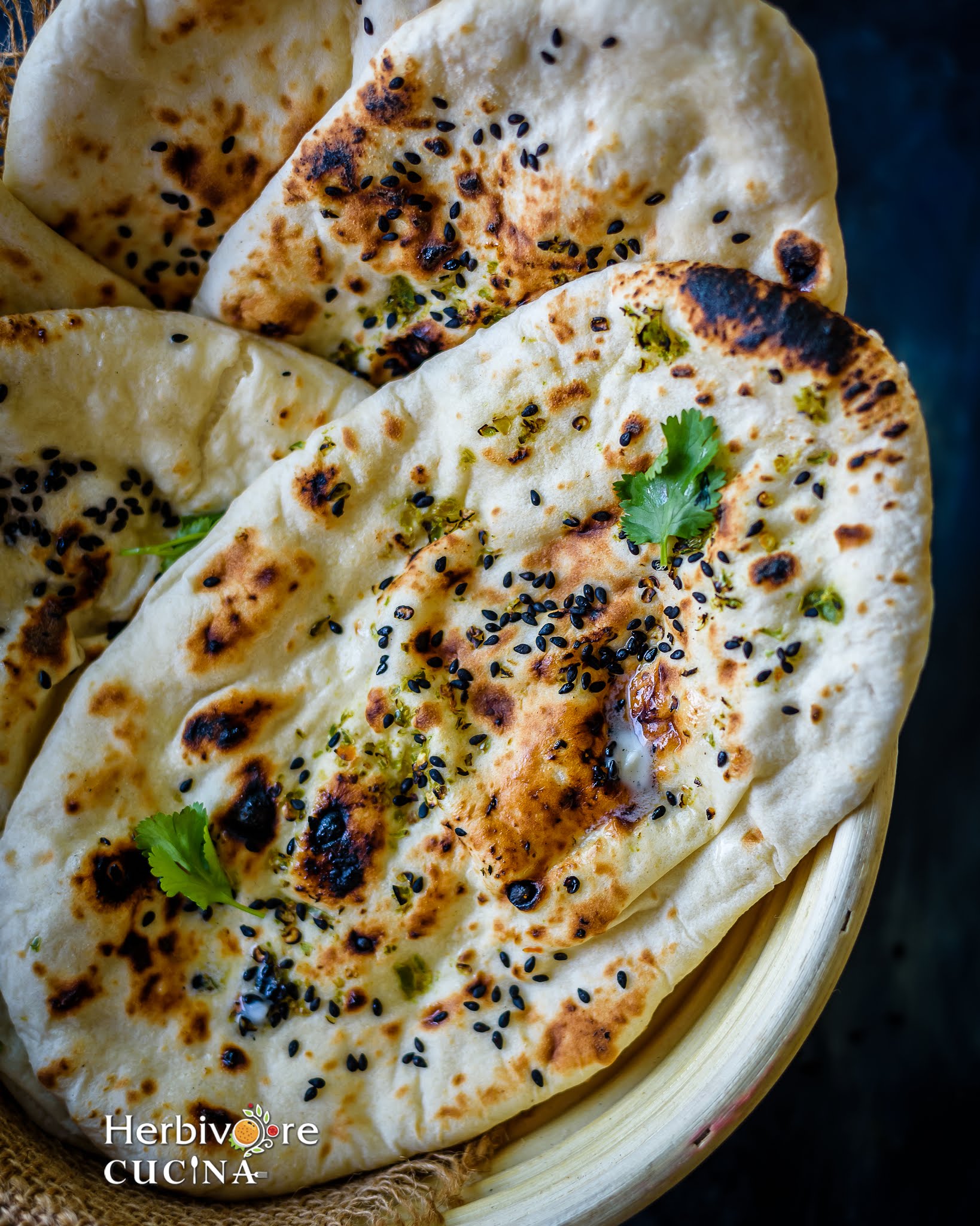 A basket with stacked sourdough naans and topped with cilantro and sesame seeds. 