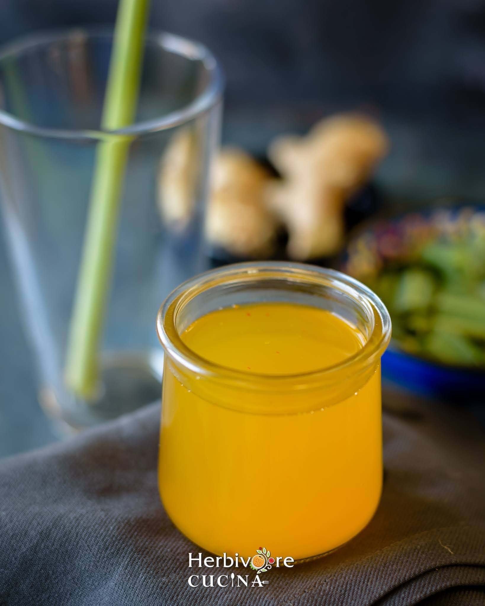A jar filled with yellow colored saffron water with some lemongrass and ginger in the background. 