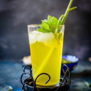 A glass filled with lemongrass ginger cooler topped with ice and mint leaves against a dark background.