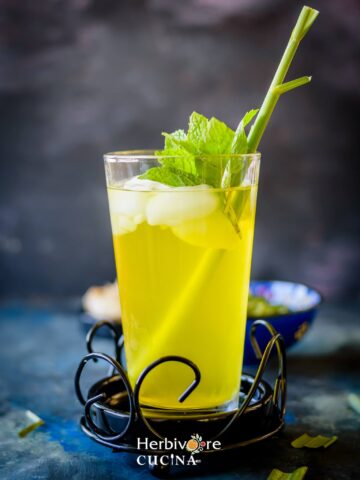 A glass filled with lemongrass ginger cooler topped with ice and mint leaves against a dark background.