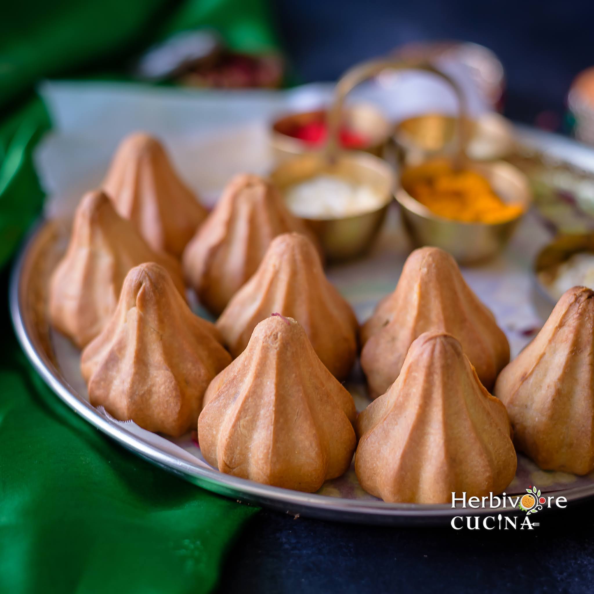 Side view of Air Fried Modaks; with puja ingredients on the back and a green napkin next to it. 