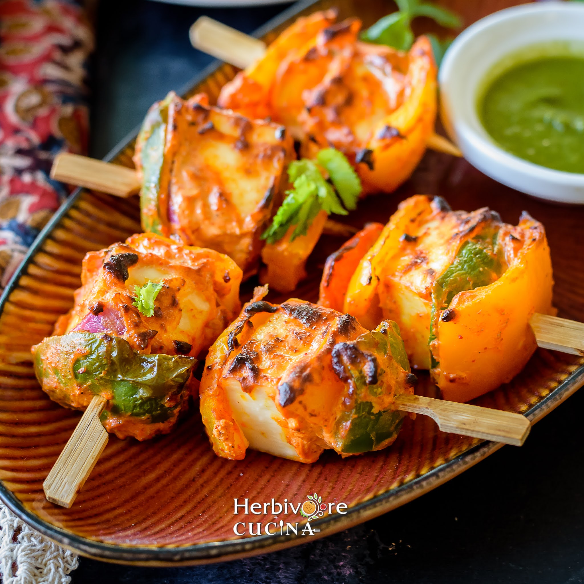 A brown platter with skewers or appetizer arranged on it with a bowl of cilantro chutney on the side. 