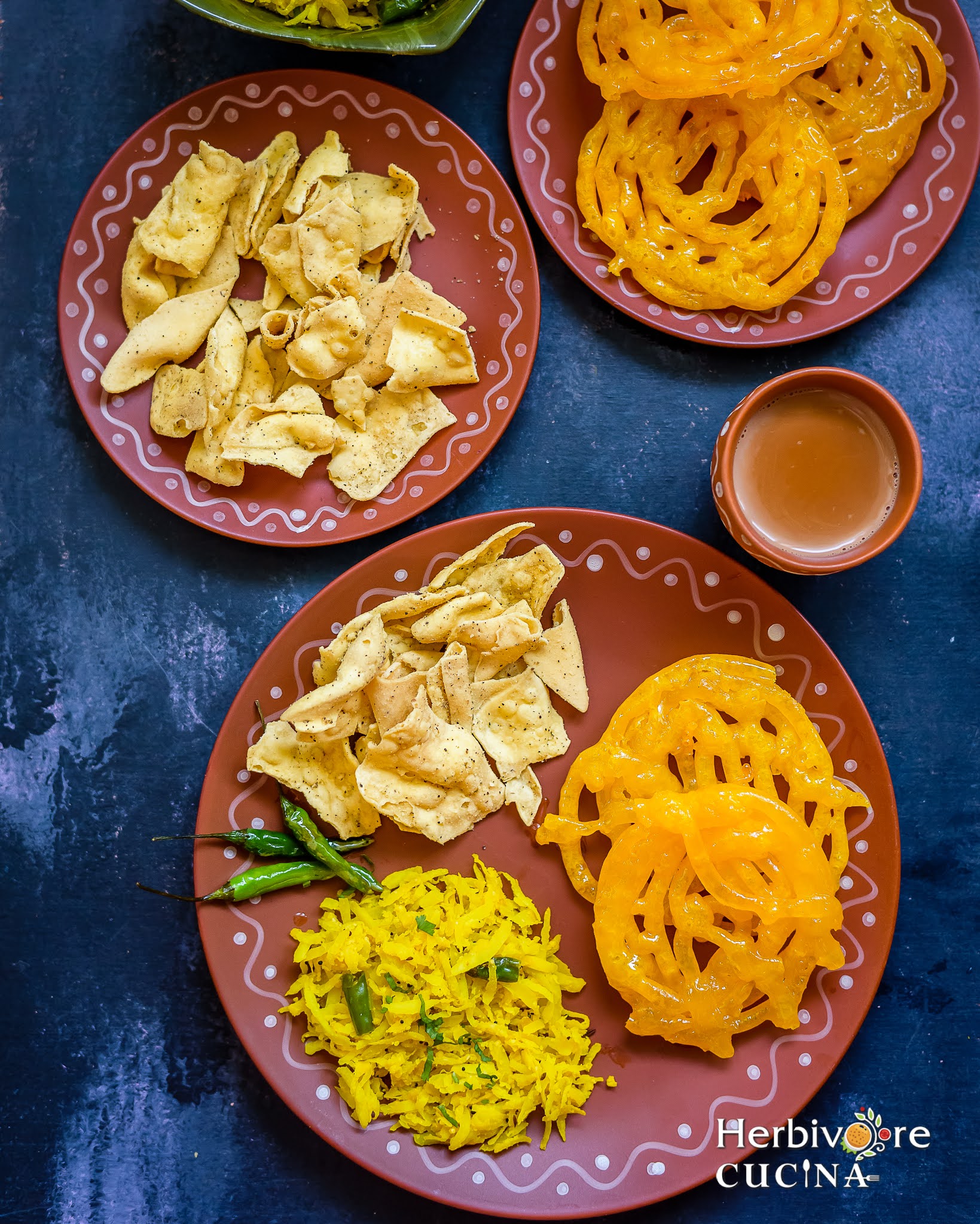 A brown plate with jalebi, fafda and papaya sambharo with masala chai on the side. 